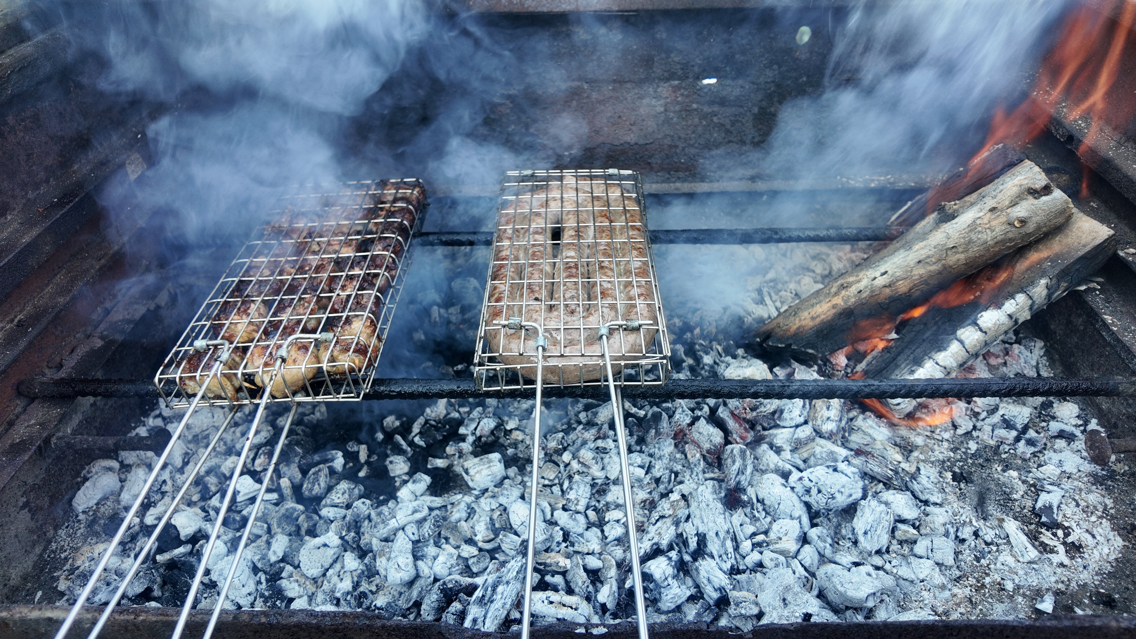 Two metal grills over glowing coals with flames and smoke in the background